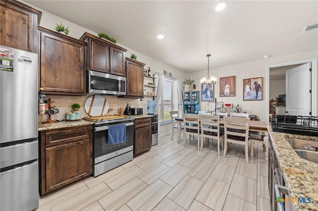 kitchen featuring stainless steel appliances, tasteful backsplash, dark brown cabinetry, an inviting chandelier, and pendant lighting