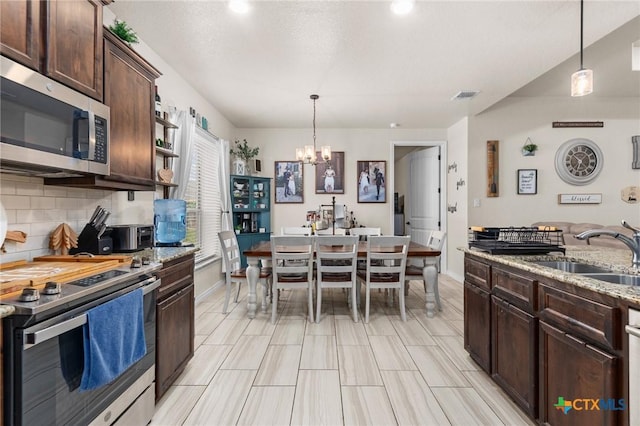 kitchen featuring stainless steel appliances, a sink, dark brown cabinets, visible vents, and a notable chandelier