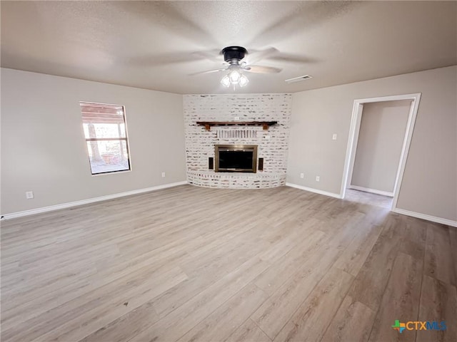 unfurnished living room featuring ceiling fan, a fireplace, light hardwood / wood-style flooring, and a textured ceiling