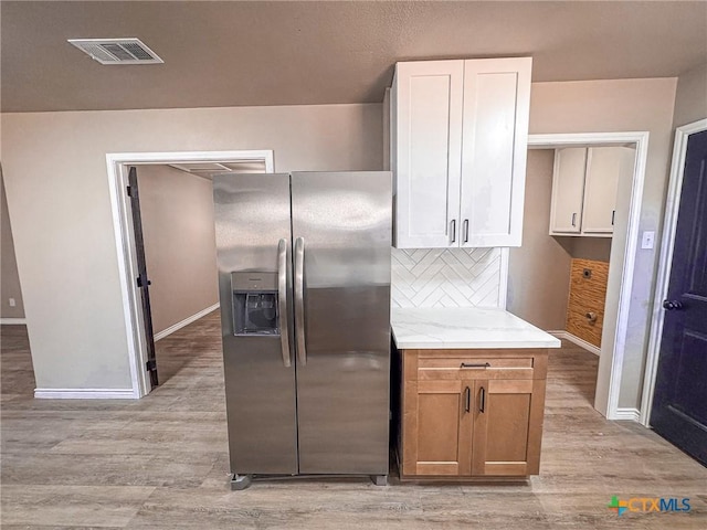 kitchen featuring tasteful backsplash, light stone counters, light wood-type flooring, stainless steel fridge, and white cabinets