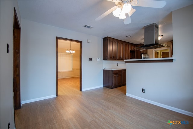 kitchen with ceiling fan with notable chandelier, island range hood, dark brown cabinetry, light wood-type flooring, and stainless steel fridge