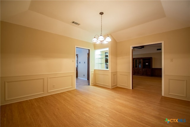 spare room featuring light hardwood / wood-style flooring, a notable chandelier, and a raised ceiling