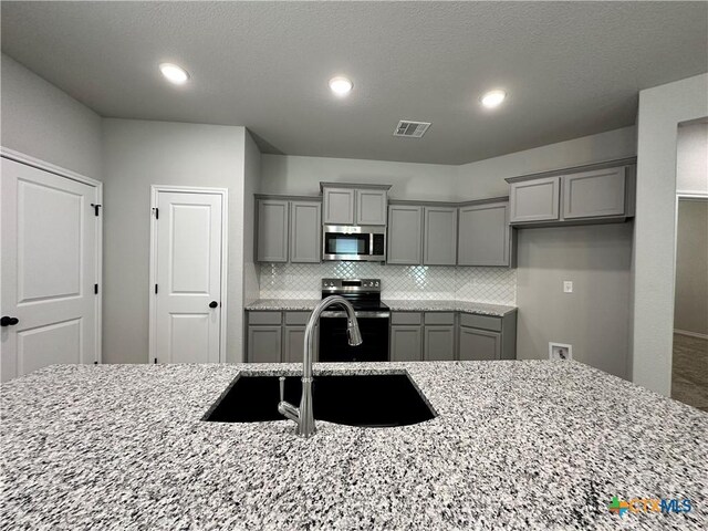 kitchen featuring an island with sink, light stone countertops, sink, and appliances with stainless steel finishes