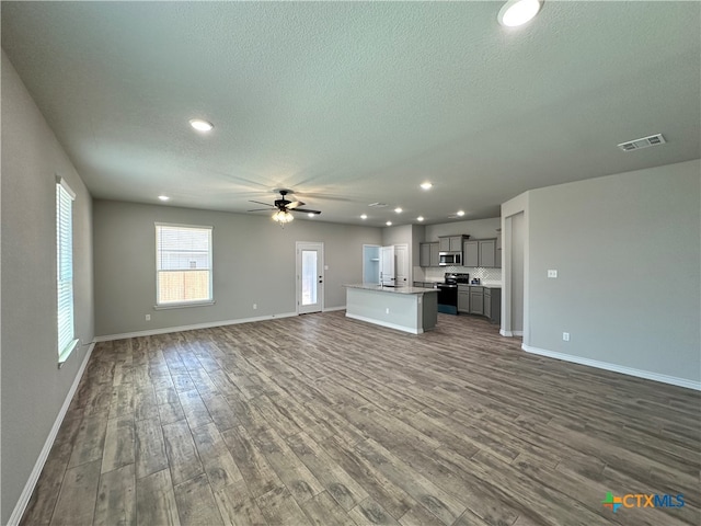 unfurnished living room featuring dark wood-type flooring, ceiling fan, and a textured ceiling