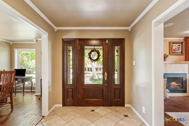 entryway with a tile fireplace, crown molding, and baseboards