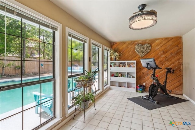 exercise room with light tile patterned flooring, wooden walls, and plenty of natural light