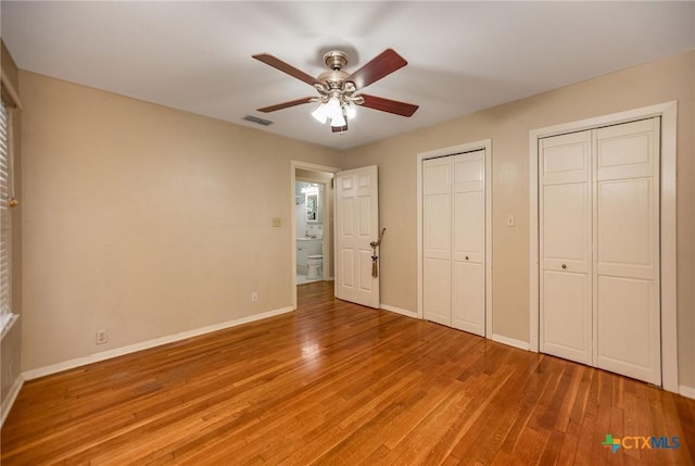 unfurnished bedroom featuring two closets, baseboards, visible vents, and light wood-style flooring
