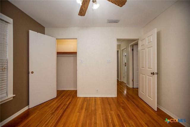 unfurnished bedroom featuring visible vents, a closet, wood finished floors, baseboards, and a ceiling fan
