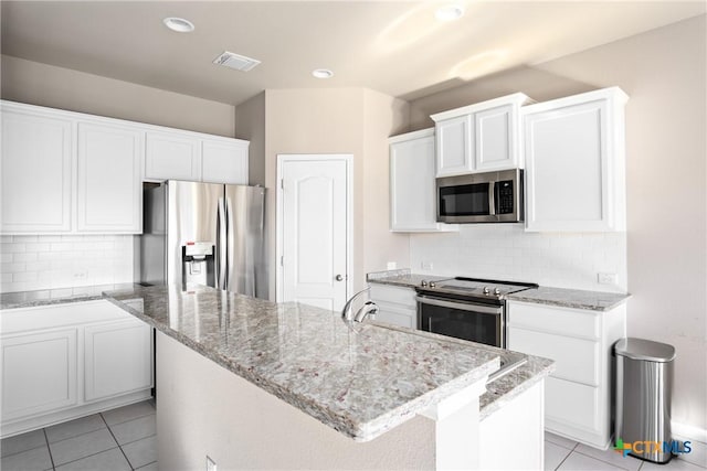 kitchen with a kitchen island with sink, light tile patterned flooring, decorative backsplash, white cabinets, and appliances with stainless steel finishes