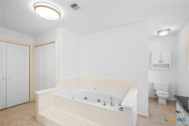 bathroom featuring tile patterned flooring, vanity, tiled bath, and toilet