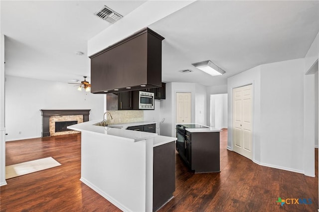 kitchen featuring ceiling fan, stainless steel microwave, dark hardwood / wood-style flooring, a stone fireplace, and kitchen peninsula