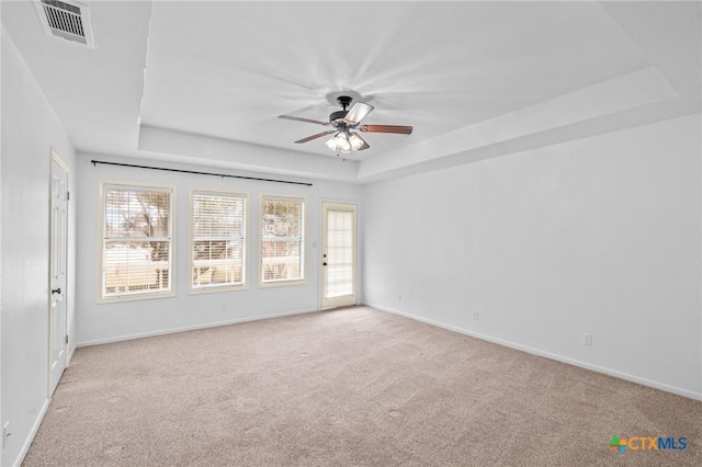 unfurnished room with a raised ceiling, light colored carpet, and ceiling fan