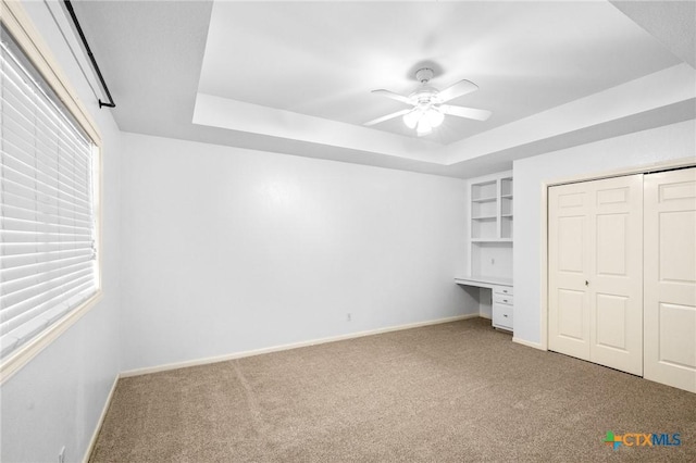 unfurnished bedroom with a raised ceiling, carpet flooring, built in desk, and a closet