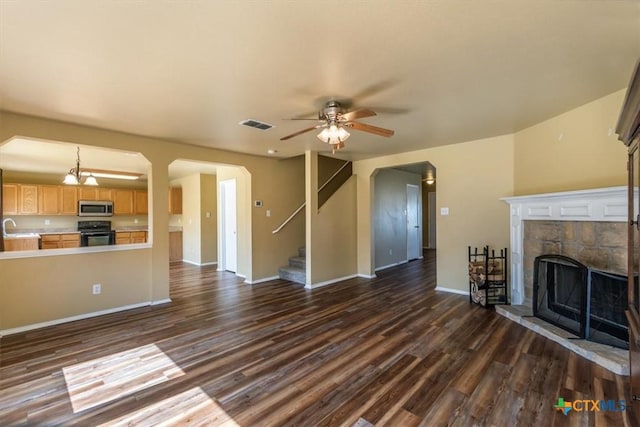 unfurnished living room featuring sink, ceiling fan, a stone fireplace, and dark wood-type flooring