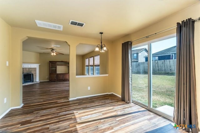 unfurnished dining area with ceiling fan with notable chandelier, dark hardwood / wood-style flooring, and a fireplace