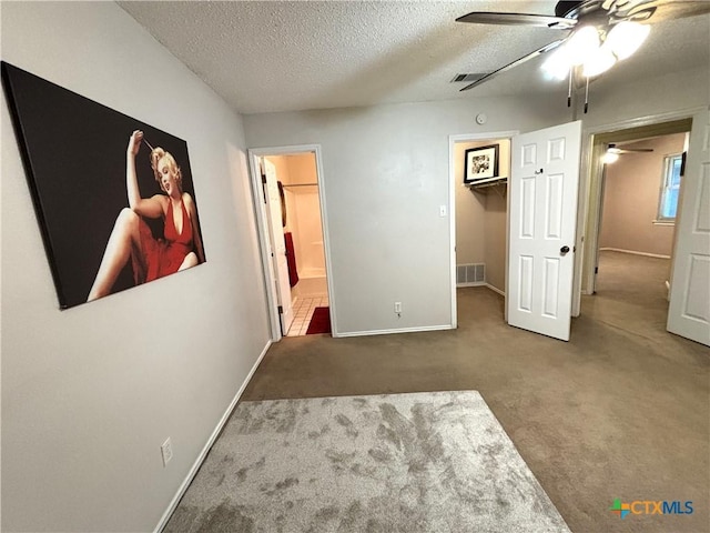 unfurnished bedroom featuring a spacious closet, visible vents, carpet floors, ensuite bath, and a textured ceiling