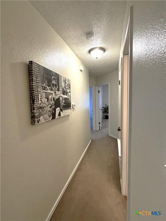 hallway featuring baseboards, carpet floors, a textured ceiling, and a textured wall