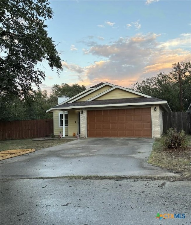 ranch-style house featuring fence, an attached garage, a chimney, concrete driveway, and brick siding