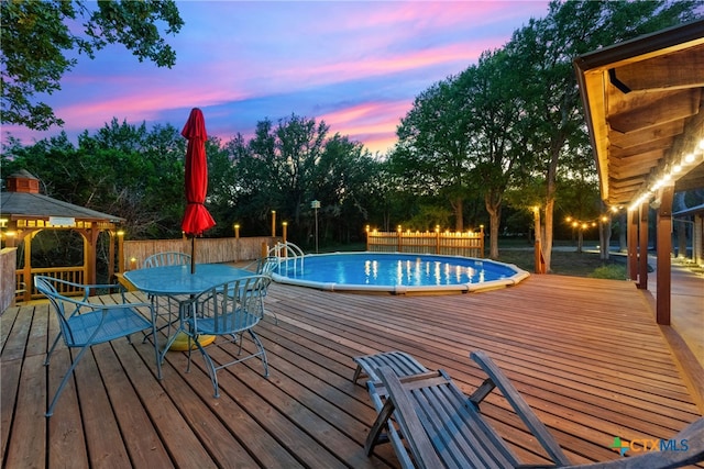 pool at dusk with a gazebo and a wooden deck