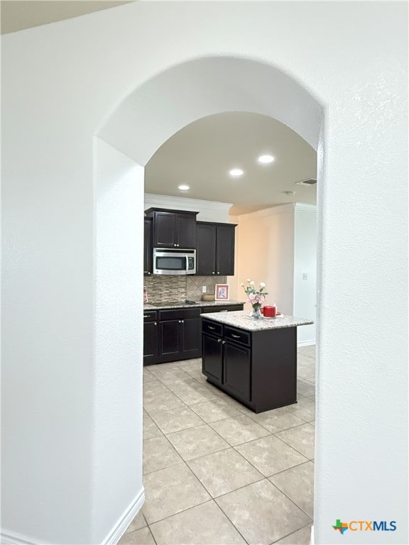 3312 Vineyard Trl, Harker Heights, TX 76548 - kitchen featuring stainless steel microwave, dark cabinetry, light tile patterned floors, backsplash, and arched walkways