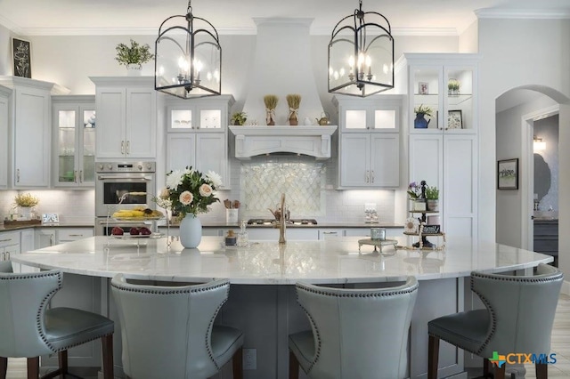 kitchen featuring a large island with sink, decorative light fixtures, and light stone countertops