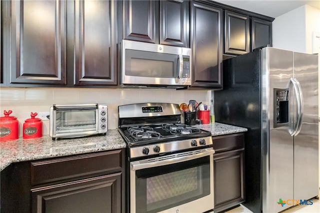 kitchen featuring decorative backsplash, a toaster, dark brown cabinetry, light stone countertops, and stainless steel appliances