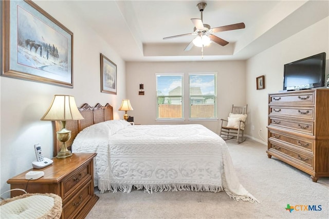 bedroom featuring a ceiling fan, a tray ceiling, and light colored carpet