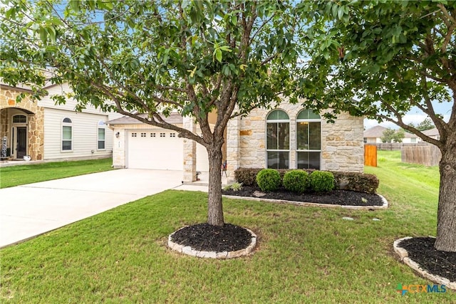 view of property hidden behind natural elements featuring a front yard, fence, concrete driveway, an attached garage, and stone siding