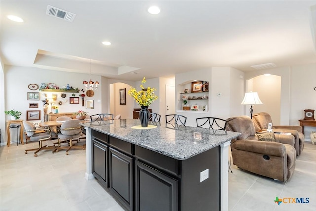 kitchen featuring a kitchen island, visible vents, arched walkways, light stone countertops, and open floor plan