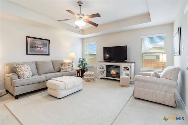 living room with baseboards, ceiling fan, and a raised ceiling
