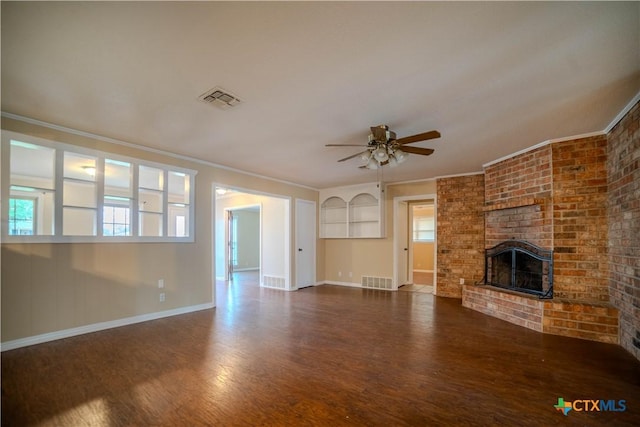 unfurnished living room with crown molding, a brick fireplace, dark wood-type flooring, and ceiling fan