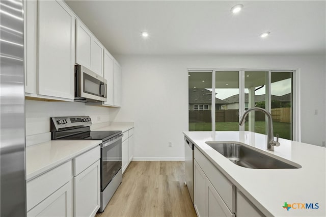 kitchen with appliances with stainless steel finishes, light wood-type flooring, white cabinetry, and sink