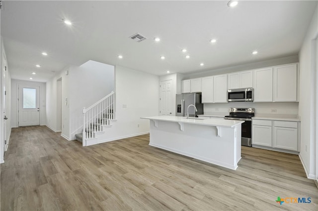 kitchen featuring a center island with sink, white cabinets, stainless steel appliances, and light hardwood / wood-style flooring