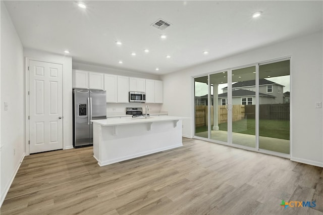 kitchen with a kitchen island with sink, light hardwood / wood-style floors, and appliances with stainless steel finishes