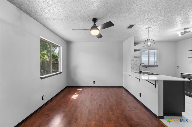 kitchen with sink, kitchen peninsula, a kitchen breakfast bar, dark hardwood / wood-style floors, and a textured ceiling