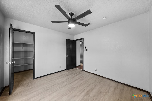 unfurnished bedroom with a walk in closet, a textured ceiling, ceiling fan, and light hardwood / wood-style flooring