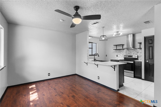 kitchen with a textured ceiling, stainless steel electric range oven, sink, a kitchen breakfast bar, and wall chimney exhaust hood