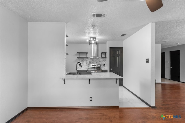 kitchen with kitchen peninsula, a textured ceiling, sink, a kitchen breakfast bar, and stainless steel electric range oven