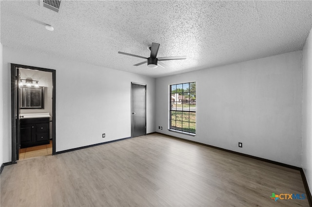 unfurnished bedroom featuring ensuite bath, a textured ceiling, and light hardwood / wood-style flooring