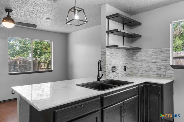 kitchen with backsplash, hanging light fixtures, sink, dark wood-type flooring, and kitchen peninsula