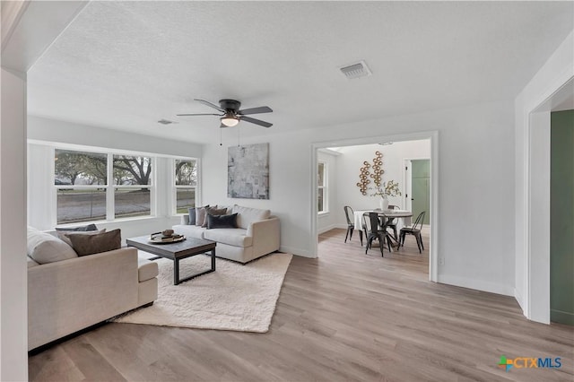 living room with visible vents, a ceiling fan, a textured ceiling, wood finished floors, and baseboards