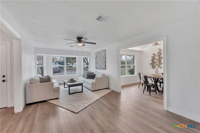 living room with visible vents, baseboards, light wood-style flooring, a textured ceiling, and a ceiling fan
