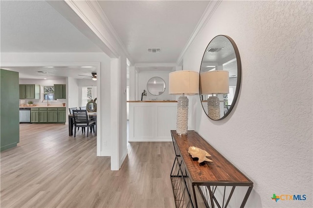 hallway with visible vents, light wood finished floors, ornamental molding, a sink, and a textured wall