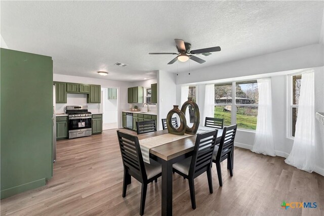 dining area with a ceiling fan, baseboards, visible vents, light wood-style floors, and a textured ceiling