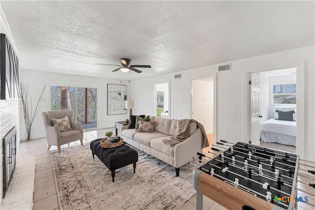 living room featuring ceiling fan, a fireplace, visible vents, and a textured ceiling