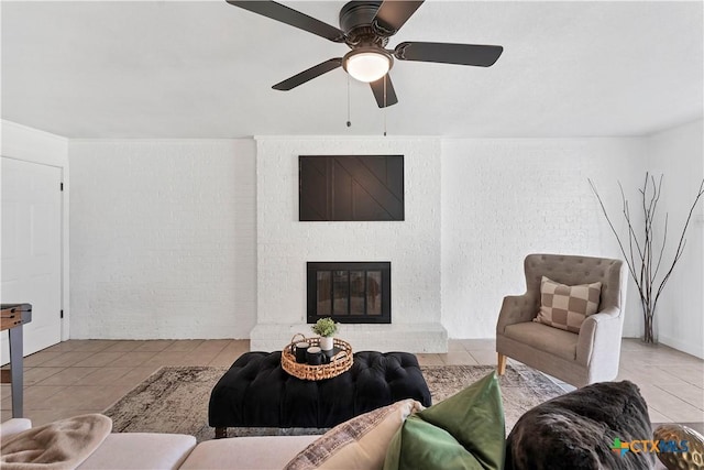 living room featuring ceiling fan, a brick fireplace, brick wall, and tile patterned flooring