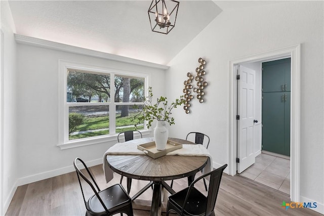 dining area with an inviting chandelier, baseboards, light wood-style floors, and lofted ceiling