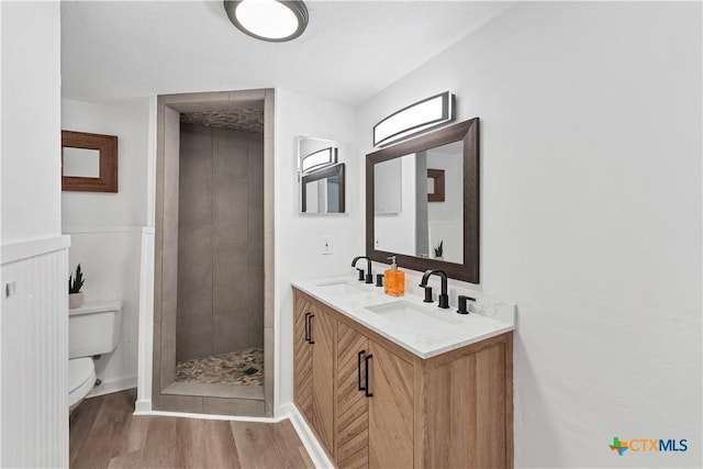 full bathroom featuring double vanity, wood finished floors, a tile shower, and a sink