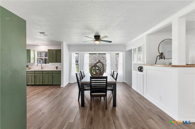 dining area featuring a ceiling fan, wood finished floors, visible vents, and a textured ceiling