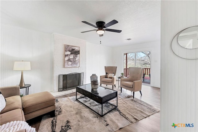 living area featuring wood finished floors, visible vents, ceiling fan, a textured ceiling, and a large fireplace